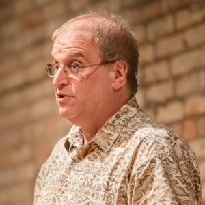 Photo of Jim Perlman, a light-skinned man with glasses, wearing a patterned tan shirt. 