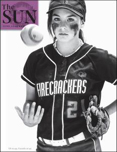 Photograph of a white girl in a baseball uniform that reads "Firecrackers," tossing a ball in the air.